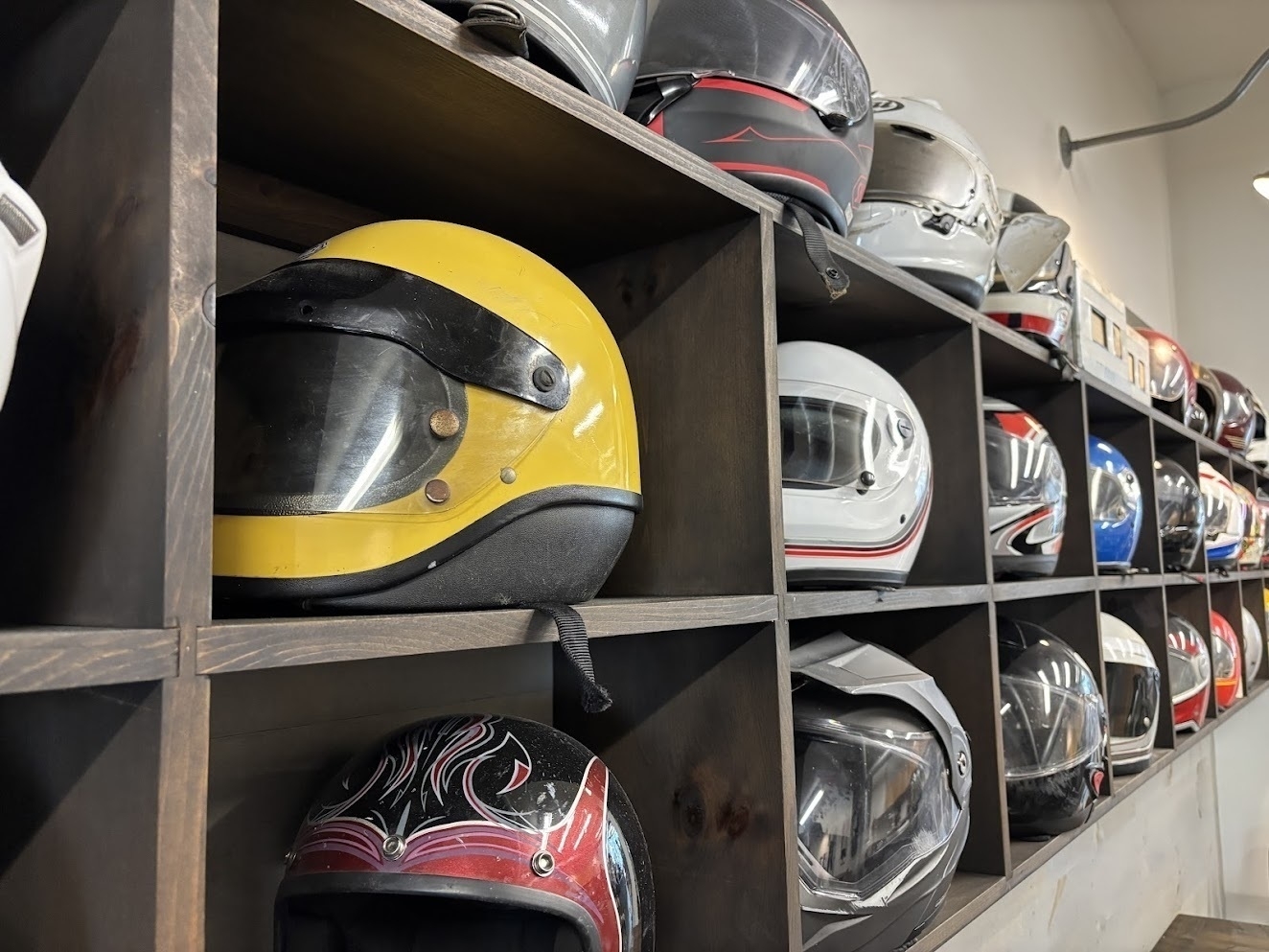 A variety of motorcycle helmets are neatly arranged in wooden cubby shelves.